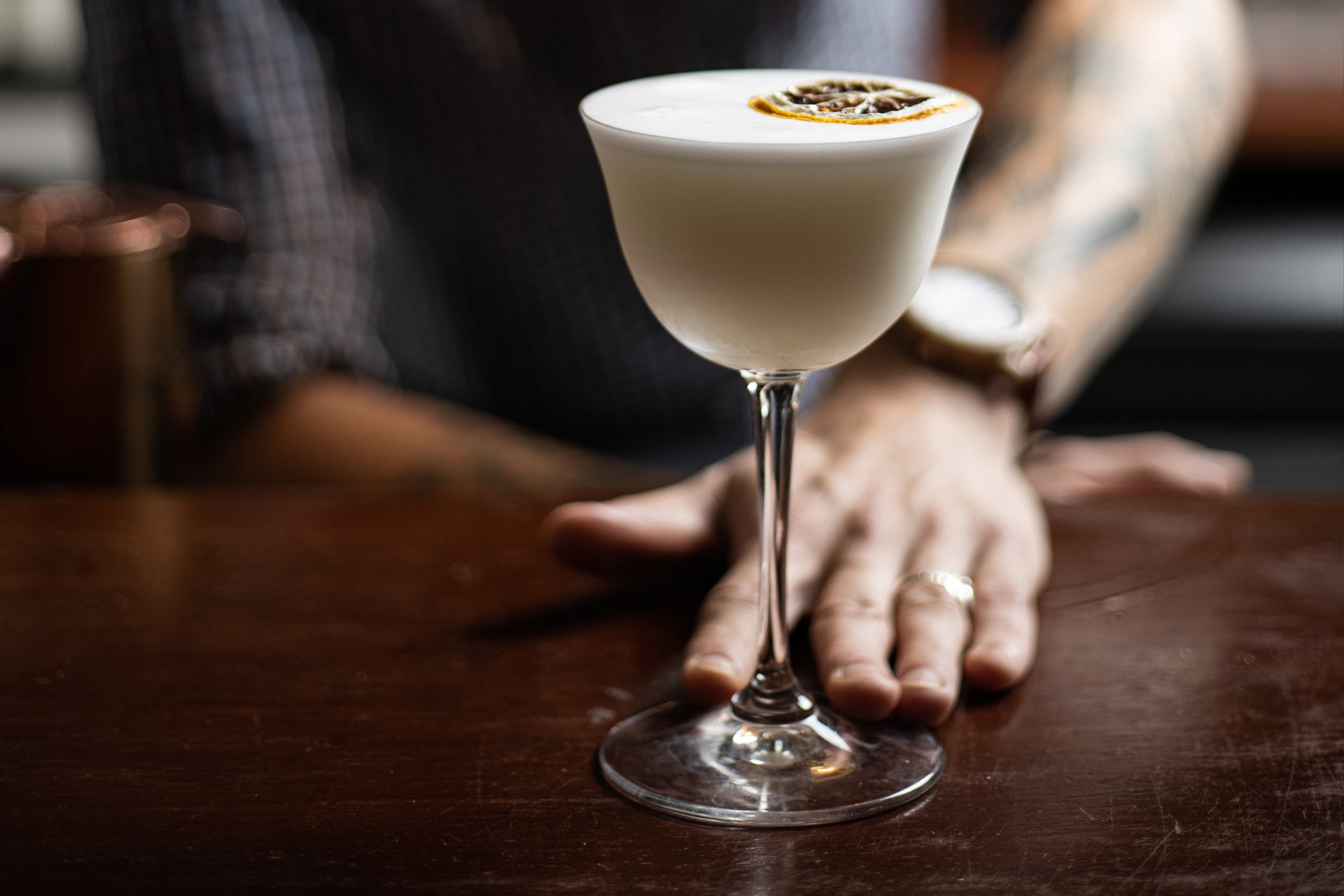 Cocktail with frothy head and garnish, presented by a bar tender